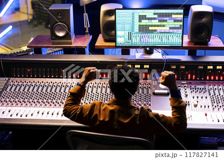Confident sound engineer finishing a new hit song in professional music studio, working with digital software on pc and console in control room. African american producer creating records with gear. Confident sound engineer finishing a new hit song in professional music studio, working with digital software on pc and console in control room. African american producer creating records with gear. 117827141
