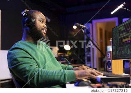 Sound designer working in home studio with digital audio software on pc, playing piano keys and editing old recordings. Artist producer creating songs on midi controller keyboard notes. 117827213