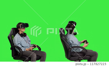 Woman celebrating her championship win with vr headset and controller, playing video games cyber space tournament against greenscreen backdrop. Gamer feeling cheerful about victory. Camera B. Woman celebrating her championship win with vr headset and controller, playing video games cyber space tournament against greenscreen backdrop. Gamer feeling cheerful about victory. Camera B. 117827223