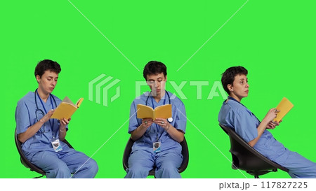 Health specialist is reading a literature book to acquire physician specialization and surgeon expertise, sitting in a chair. Nurse studying healthcare industry lecture against greenscreen. Camera B. Health specialist is reading a literature book to acquire physician specialization and surgeon expertise, sitting in a chair. Nurse studying healthcare industry lecture against greenscreen. Camera B. 117827225