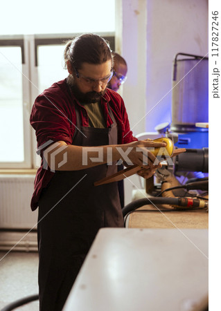 Artisan with safety glasses next to apprentice using sanding block to remove imperfections on wood piece. Creative man wearing protective gear enjoying diy hobby, using sandpaper to do sanding Artisan with safety glasses next to apprentice using sanding block to remove imperfections on wood piece. Creative man wearing protective gear enjoying diy hobby, using sandpaper to do sanding 117827246