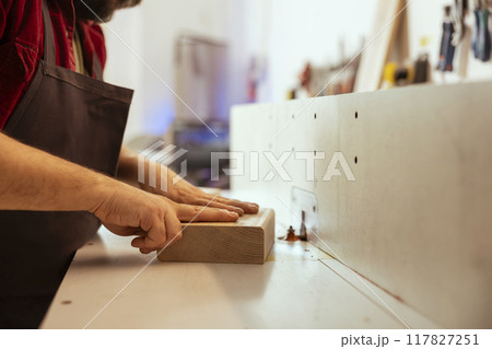 Woodworking professional operating wood shaper in assembly shop, creating intricate designs with precision. Cabinetmaker uses spindle moulder to shape and mold wooden pieces, close up shot Woodworking professional operating wood shaper in assembly shop, creating intricate designs with precision. Cabinetmaker uses spindle moulder to shape and mold wooden pieces, close up shot 117827251