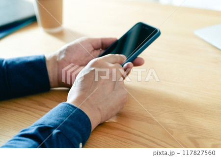 机の上でスマホを使う男性の手元 117827560
