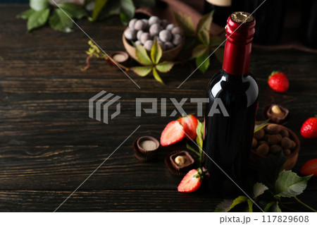 A bottle of wine on a dark, wooden table with flowers. 117829608