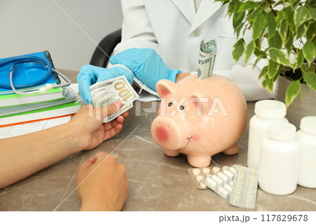 A doctor with a piggy bank on the table, the concept of corruption in medicine. A doctor with a piggy bank on the table, the concept of corruption in medicine. 117829678