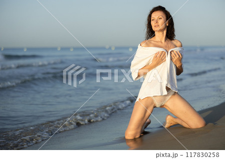 Topless woman in white shirt kneeling on coast Topless woman in white shirt kneeling on coast 117830258