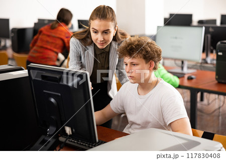 Female teacher helping focused teenage student in computer lab 117830408