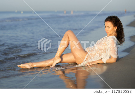 Woman in white negligee lies on coast Woman in white negligee lies on coast 117830558