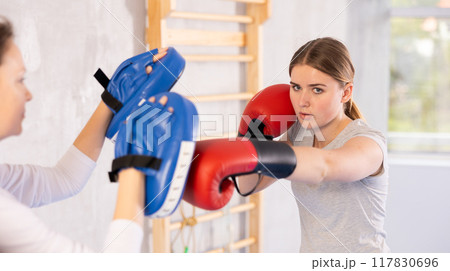 Girl teenager with her trainer in gym learns to hit punch mitts 117830696