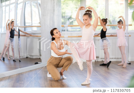 Ballet lesson for little girls - choreography teacher shows little ballerinas how to get into different poses correctly in sturio 117830705