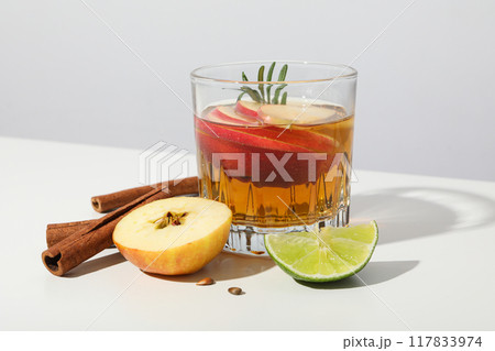 Glass with apple cider, cinnamon sticks, lime and apple pieces on white background, close up 117833974