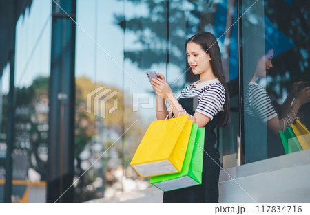 A woman is standing outside with a cell phone in her hand A woman is standing outside with a cell phone in her hand 117834716