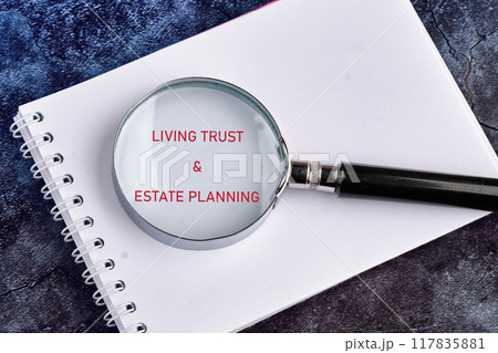 LIVING TRUST and ESTATE PLANNING written through a magnifying glass in a notebook on a dark background 117835881