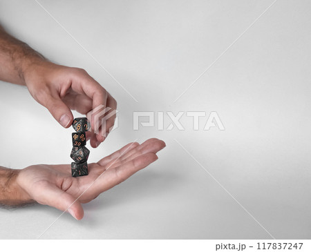 Hands rolling unique polyhedral dice in mid-air against a minimalistic background 117837247