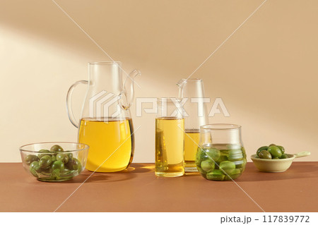 Front view of fresh olives decorated with glass flasks containing olive oil on beige background. Scene for display of organic cosmetic products with olive extract 117839772
