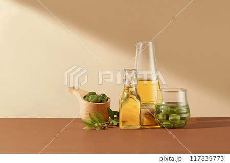 Minimal scene for advertising. Fresh olives, leaves and olive oil on glass bottles decorated on beige background. Front view, space for display product 117839773