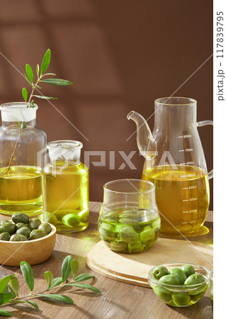 Advertising photo of nature ingredient for cosmetic product - olive. On wooden table and brown background, fresh olives decorated with glass bowls of olive oil 117839795