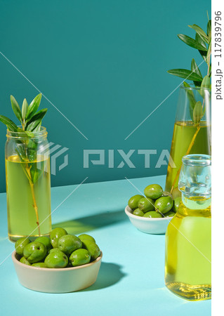 Fresh olives on ceramic bowls decorated with glass bottles of olive oil on green background. Advertising photo for cosmetic product with ingredients from olive Fresh olives on ceramic bowls decorated with glass bottles of olive oil on green background. Advertising photo for cosmetic product with ingredients from olive 117839796
