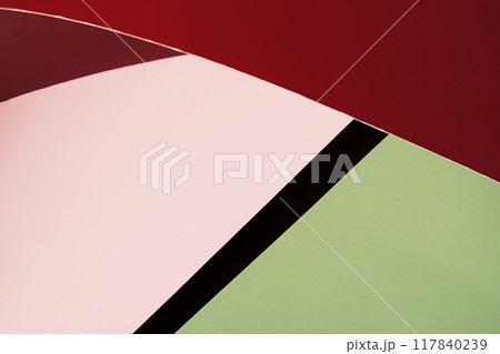 Close up of curved red and pink paper against green background. 117840239