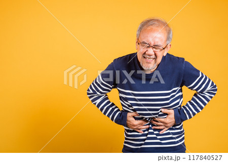 Portrait Asian old man with glasses holds hands on abdomen he stomach ache studio shot isolated yellow background, senior man pensioner feeling pain abdominal pain, hepatitis painful 117840527