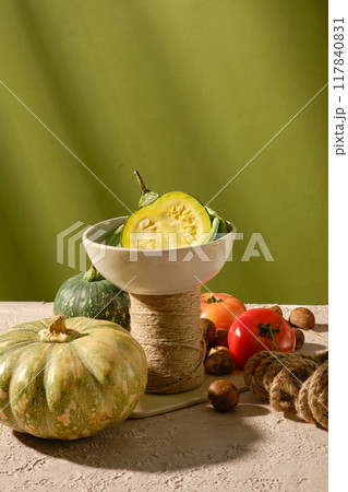 Green background photo from frontal view, in the middle displaying a white ceramic bowl contains green pumpkin, surrounded with fresh vegetables for a healthy meal cooking. Space for text 117840831