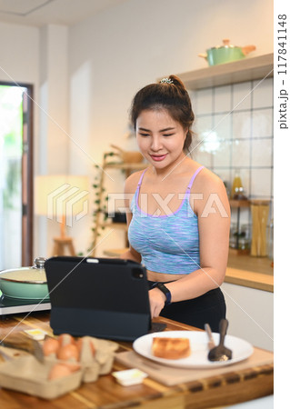 Beautiful young woman following an online recipe on digital tablet while cooking in domestic kitchen 117841148