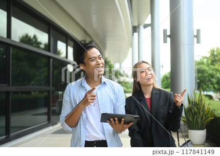 Two businesspeople with friendly conversation walking together outside an office building Two businesspeople with friendly conversation walking together outside an office building 117841149