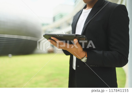 Cropped shot of young businessman standing outside office building and using digital tablet Cropped shot of young businessman standing outside office building and using digital tablet 117841155