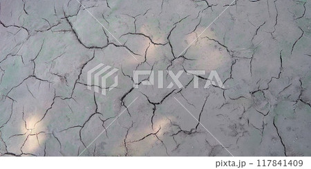 Sun beams on dry cracked gray ground, shadow close-up 117841409