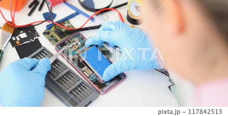 Hands with tweezers repairing a battery from a smartphone Hands with tweezers repairing a battery from a smartphone 117842513