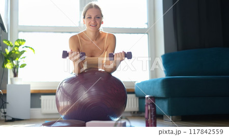 Woman doing exercises with dumbbells on a burgundy ball 117842559