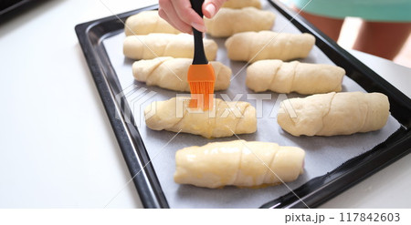 A woman's hand is brushing yolk on buns of dough 117842603