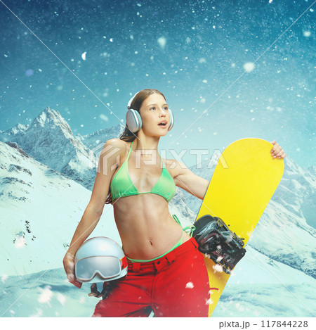 Young girl, snowboarder confidently posing with gear in winter landscape, dressed in bikini top, blending cold of winter with bold fashion statement. Young girl, snowboarder confidently posing with gear in winter landscape, dressed in bikini top, blending cold of winter with bold fashion statement. 117844228