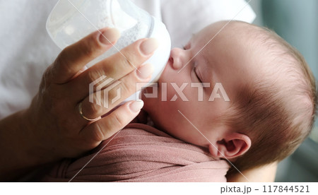 Mother Feeds Newborn Baby Formula From A Bottle As The Infant Consumes It Mother Feeds Newborn Baby Formula From A Bottle As The Infant Consumes It 117844521