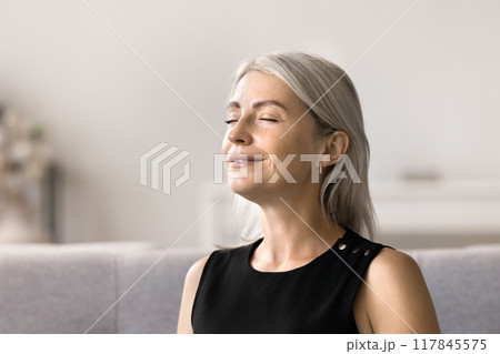 Woman closing her eyes resting seated on sofa at home 117845575