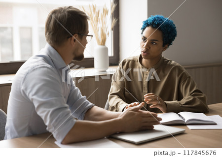 Attractive blue-haired African employee lead talk to male colleague Attractive blue-haired African employee lead talk to male colleague 117845676