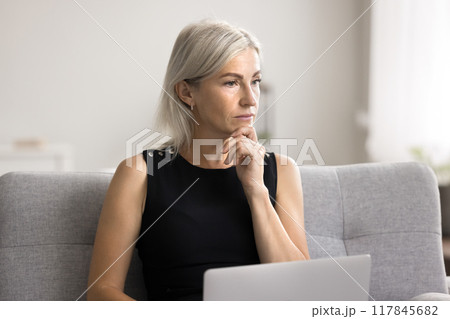 Puzzled mature woman sit on sofa with laptop Puzzled mature woman sit on sofa with laptop 117845682