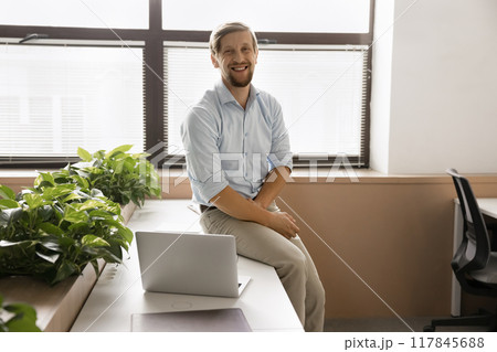 Office employee sits on table in coworking space with laptop Office employee sits on table in coworking space with laptop 117845688