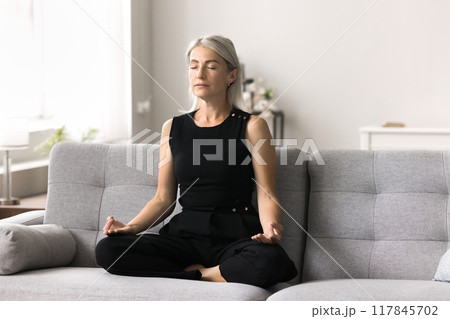 Mature peaceful woman relaxing, meditating at home 117845702