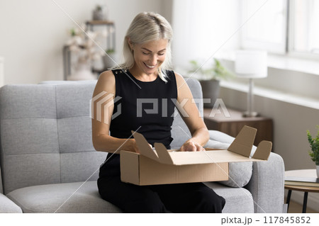 Woman sit on sofa open parcel box with bought goods Woman sit on sofa open parcel box with bought goods 117845852