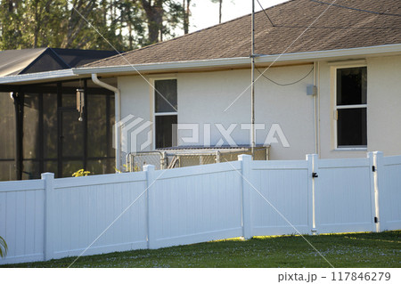 White vinyl picket fence on green lawn surrounding property grounds for backyard protection and privacy White vinyl picket fence on green lawn surrounding property grounds for backyard protection and privacy 117846279