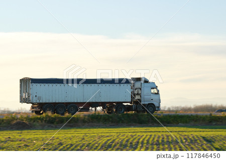 Semi-truck with tipping cargo trailer transporting sand from quarry driving on highway hauling goods in evening. Delivery transportation and logistics concept 117846450
