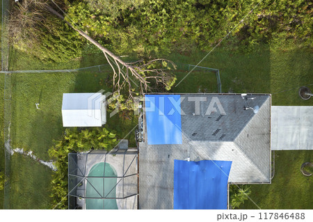 Top view of leaking house roof covered with protective tarp sheets against rain water leaks until replacement of asphalt shingles. Damage of building rooftop as aftermath of hurricane Ian in Florida 117846488