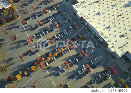 Top view of many cars parked on a parking lot in front of a strip mall plaza. Concept of consumerism and market economy 117846491