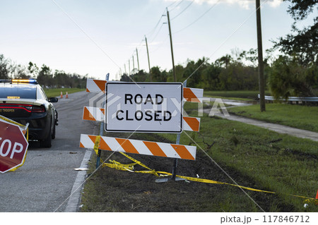 Police patrol car at yellow protective barrier at street construction site. Warning road sign about utility work 117846712