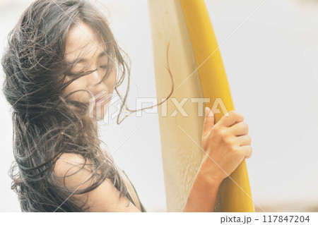 風が吹く海でサーフボードを持って立っている若い女性 117847204