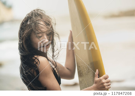 風が吹く海でサーフボードを持って立っている若い女性 風が吹く海でサーフボードを持って立っている若い女性 117847208