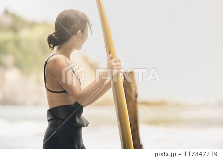 風が吹く海でサーフボードを持って立っている若い女性 風が吹く海でサーフボードを持って立っている若い女性 117847219