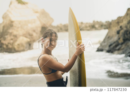 風が吹く海でサーフボードを持って立っている若い女性 117847230