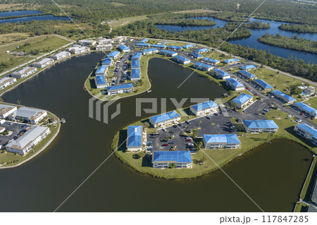 Aerial view of damaged in hurricane apartment building roofs covered with blue protective tarp against rain water leaking until replacement of asphalt shingles 117847285